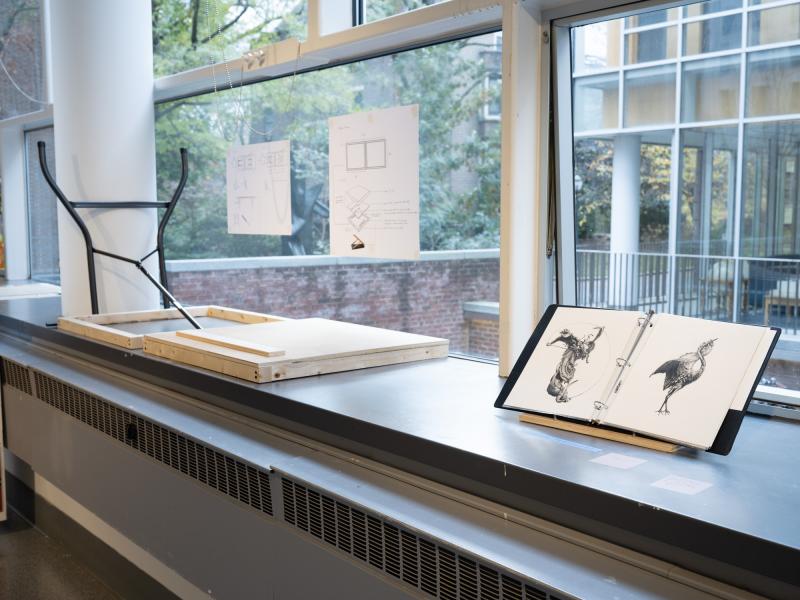 a table and open book of drawings on a window sill