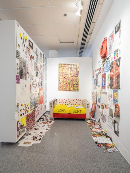 installation image of multiple prints, drawings and paintings installed in a confined space with a painted couch