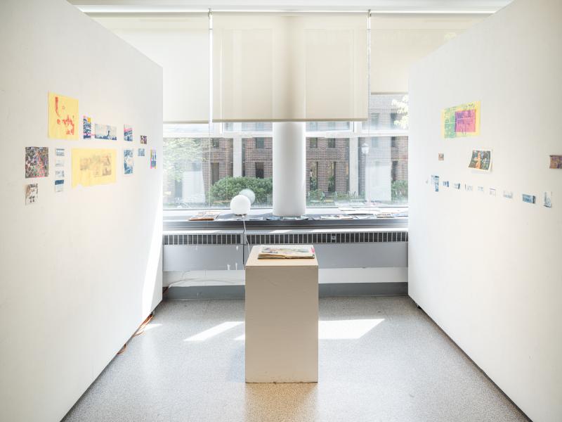 multiple prints and a book on a pedestal installed in a gallery
