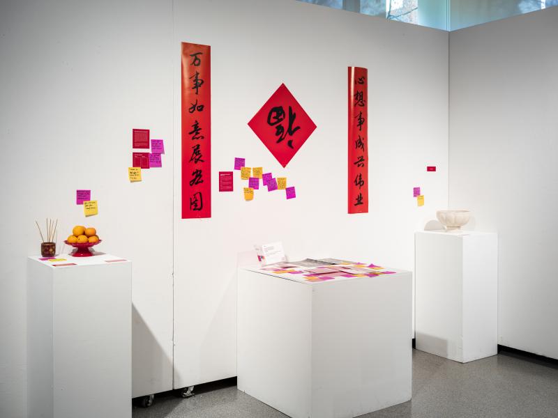 installation of wall hung posters, Post-It notes, and oranges, incense, and candy on pedestals