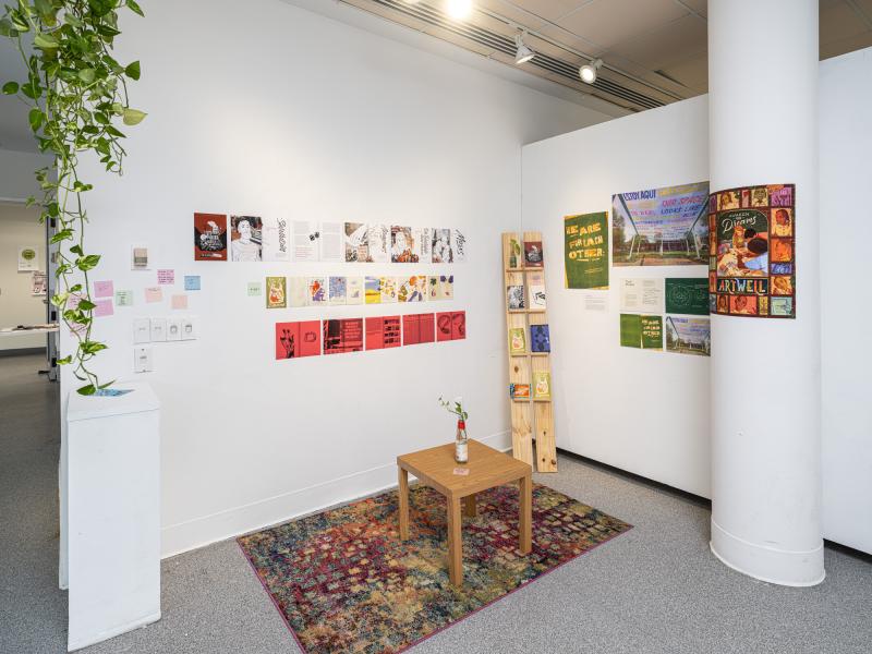 corner installation with multiple printed materials, books, posters, and a table on a rug