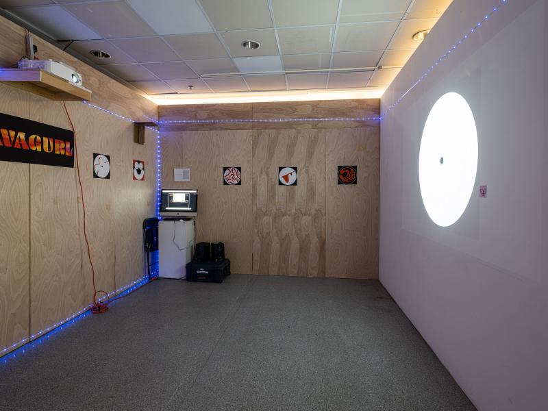 installation of posters, computer monitor, and video projection in a dark interior