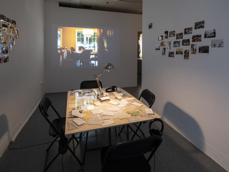 installation image of table filled with recipe cards, photos on the walls, and video projection  