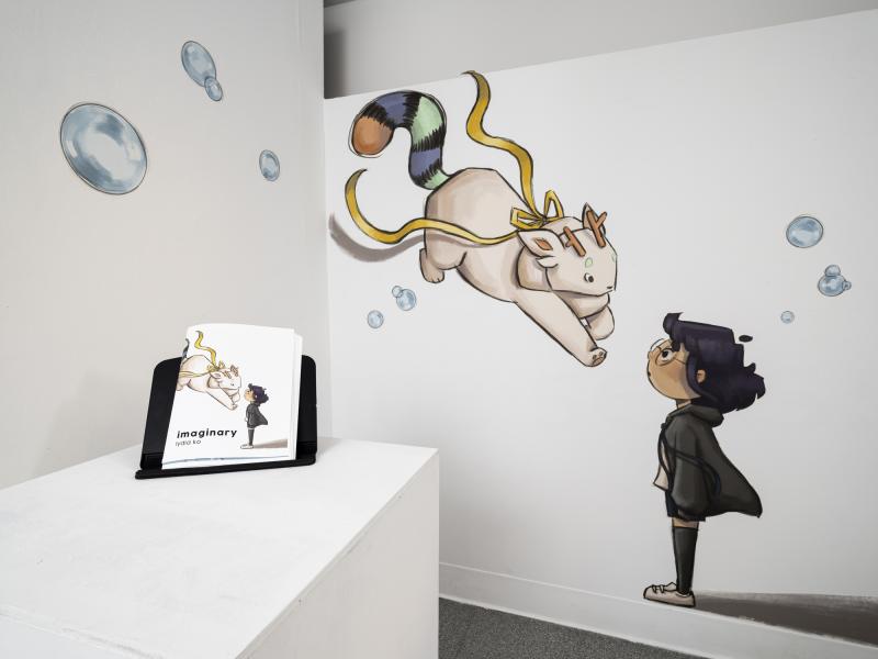 installation image of illustrations on walls and a book on a pedestal