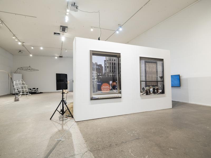 installation image with two large photographs, A/V equipment, and floor sculptures