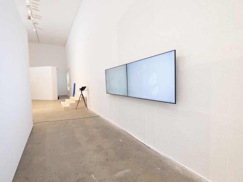 installation image with two wall hung monitors and floor sculptures in the background