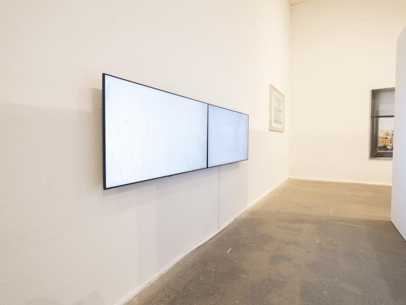 installation image with two wall hung monitors and large scale photographs in the background