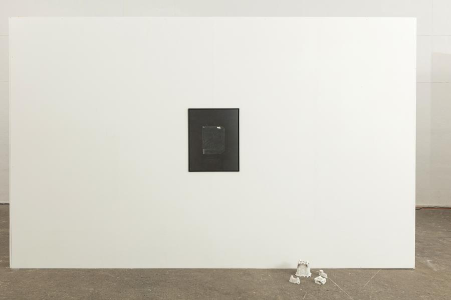 Image of black and white framed photograph with small sculptures on the floor to the right
