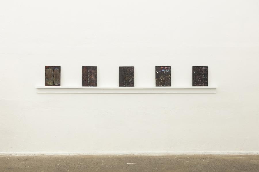 Image of five rectangular, darkly fired, ceramic pieces evenly spaced on wall shelf 