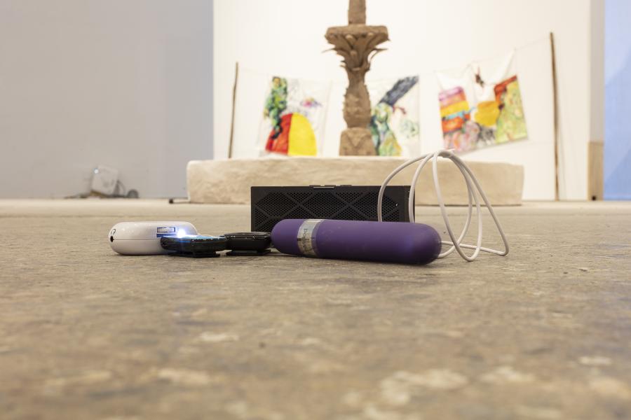 Image of small floor sculpture consisting of a purple vibrator, portable speaker, and electronic devices