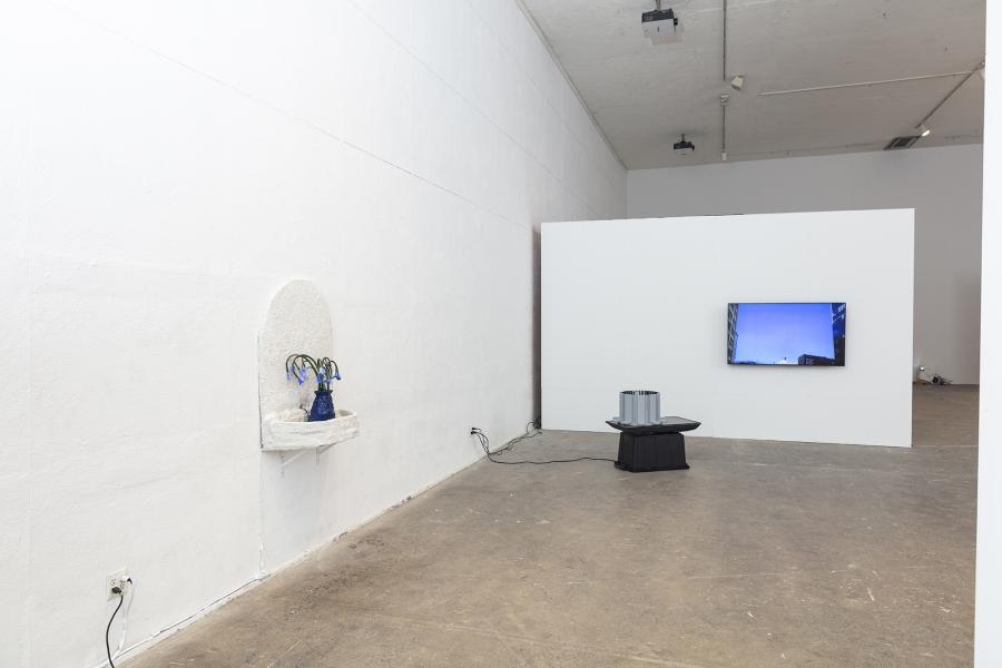 installation image with a wall fountain on the left, sculpture with monitor on the floor, and video monitor on the wall