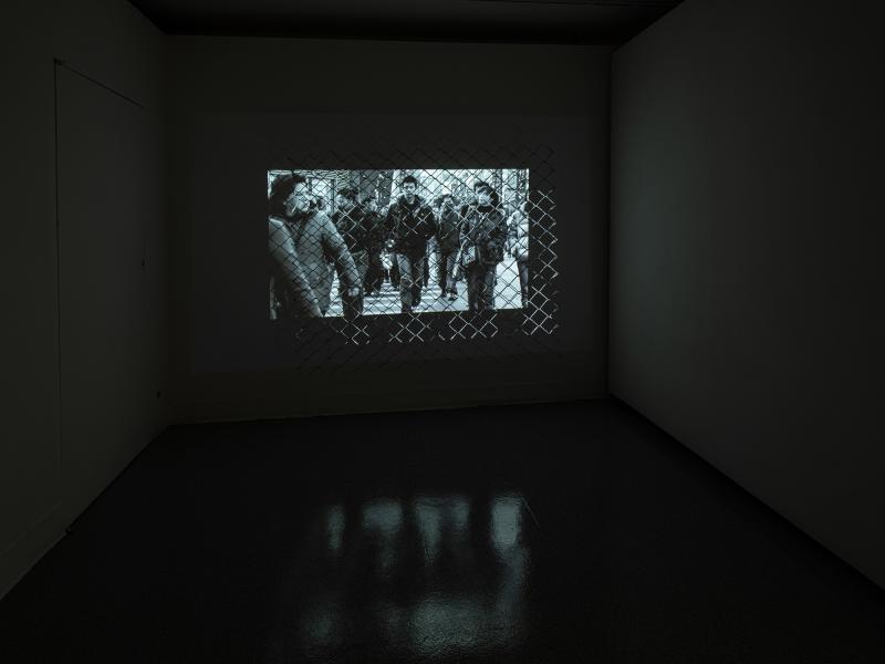 video artwork projected through a metal fence in a darkened gallery space