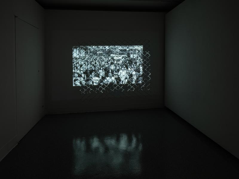 video artwork projected through a metal fence in a darkened gallery space