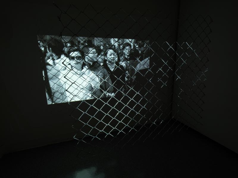 video artwork projected through a metal fence in a darkened gallery space