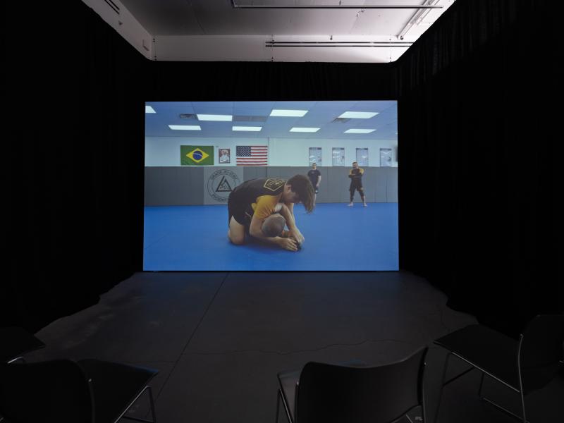 installation image of a video projection and chairs in a darkened gallery space