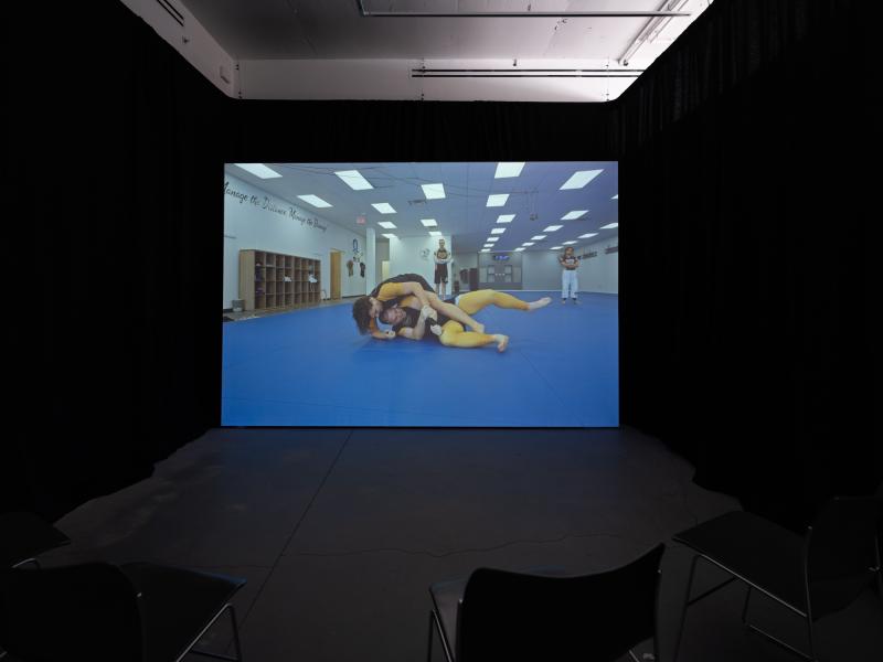 installation image of a video projection and chairs in a darkened gallery space