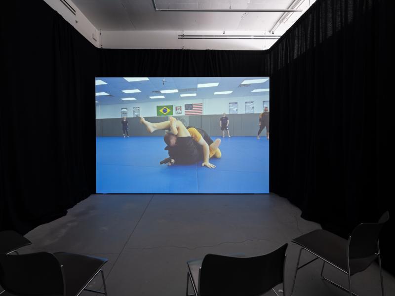 installation image of a video projection and chairs in a darkened gallery space