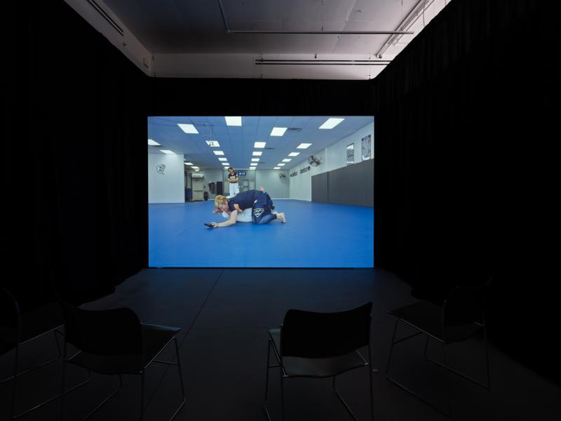 installation image of a video projection and chairs in a darkened gallery space