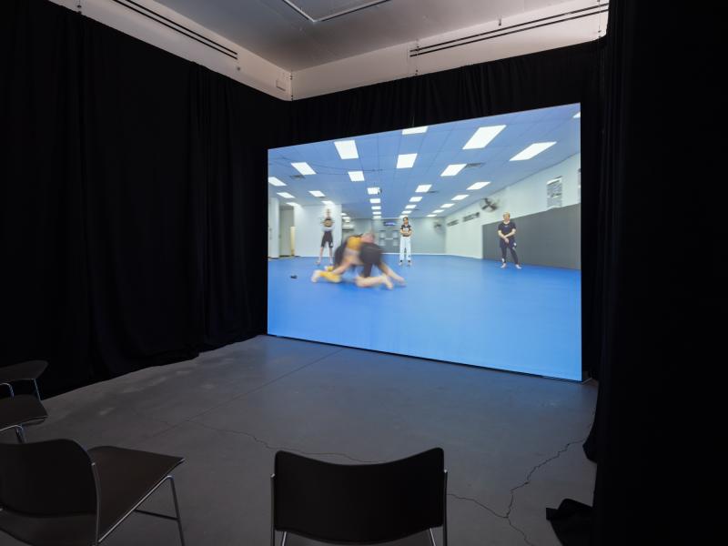 installation image of a video projection and chairs in a darkened gallery space