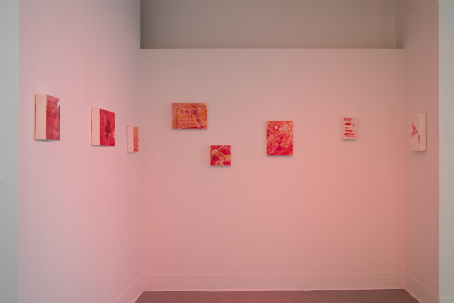 installation of several small paintings installed in a corner with red lighting