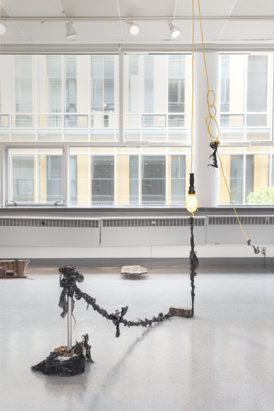 large mixed media sculpture installed on the floor and attached to the ceiling with light bulbs and cords