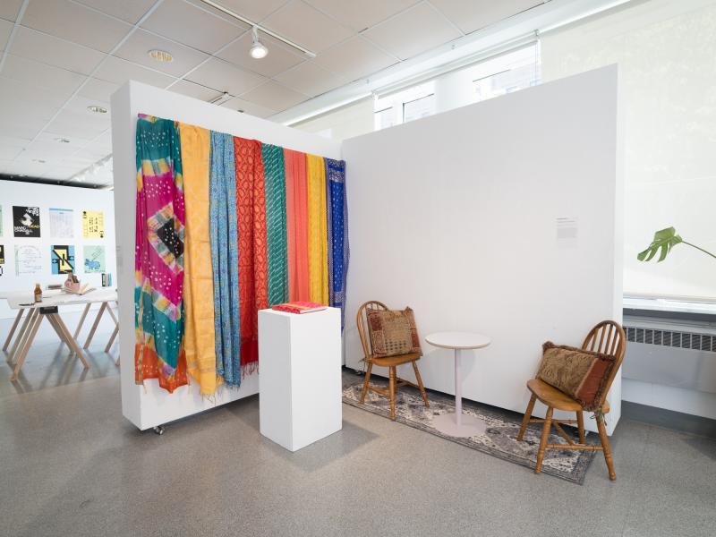 installation image of multiple fabrics installed on a wall, chairs with a side table, and a book on a pedestal