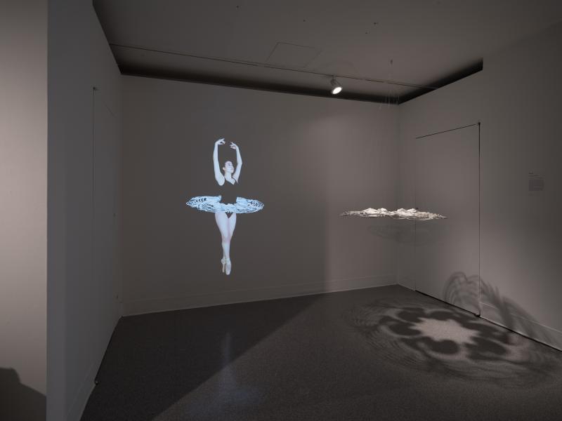 installation image of dark space with projection and a sculpture suspended from the ceiling