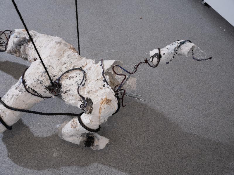 detail of a mixed media figurative sculpture suspended from a gallery ceiling