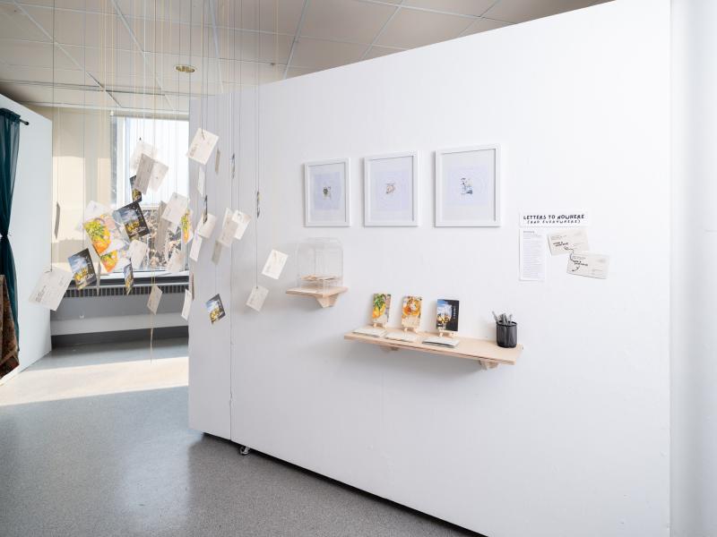 multi media installation with framed images, cards on a shelf and hanging from the gallery ceiling