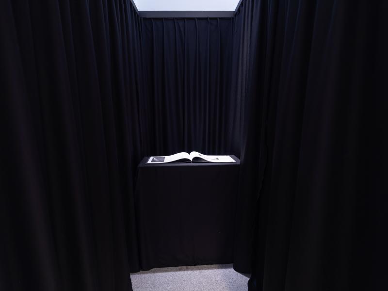 a book installed on a black pedestal in a dark space in a gallery 