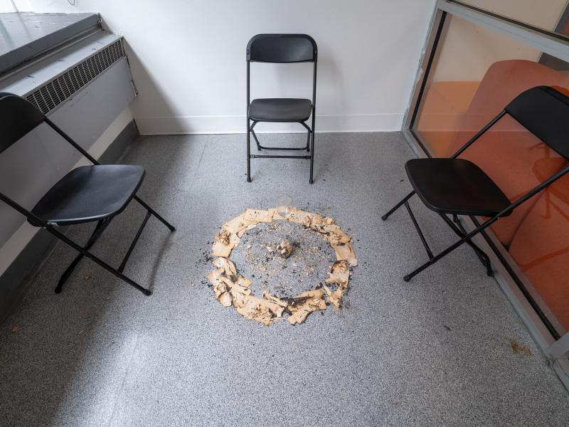 installation image of a mixed media piece installed on the floor and surrounding chairs