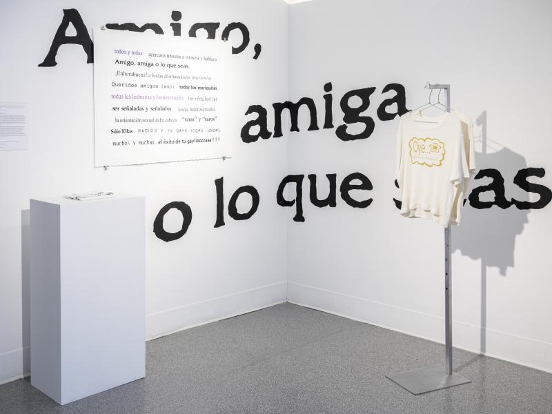 installation displaying painted wall text, poster, printed scarf and floor rack with printed shirts 