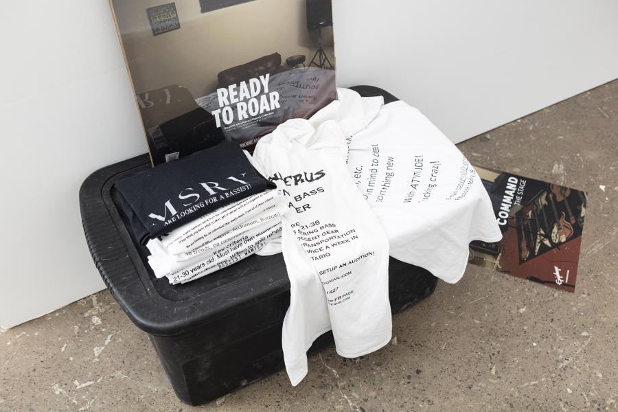 folded t-shirts and a poster on a black plastic bin on the floor