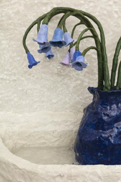 detail image of a wall mounted fountain with a dark blue vase and flowers weeping water