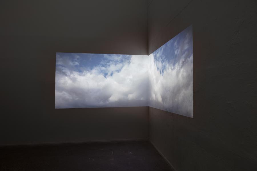 image of dual videos projected onto the corner of the gallery displaying clouds and sky