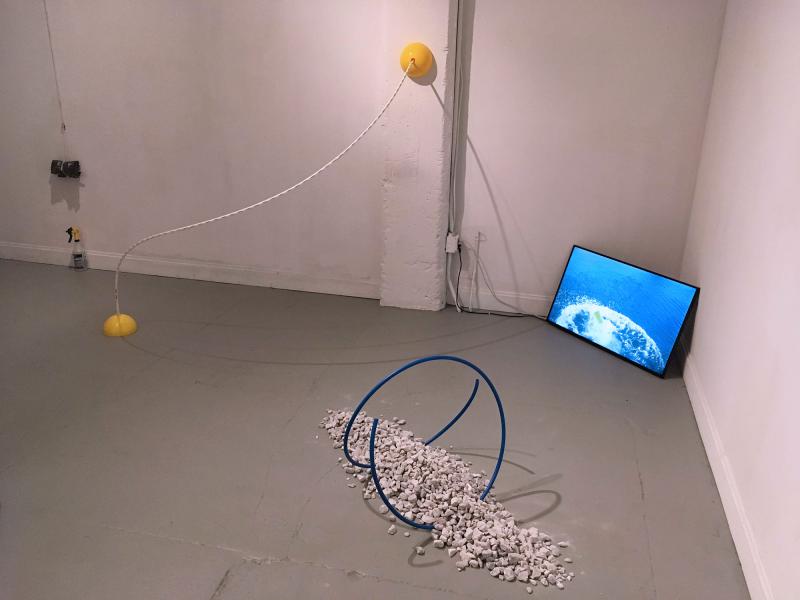 installation image of multiple pieces including sculptures on the floor and wall with a video screen on the floor in the corner