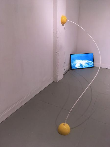 sculpture using two yellow half spheres on the floor and wall connected by a bending plastic tube, video monitor on the floor