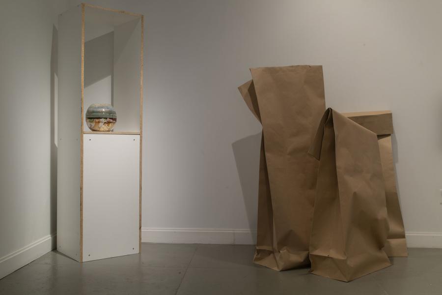 a multicolored spherical sculpture on a pedestal beside two large paper bag sculptures 