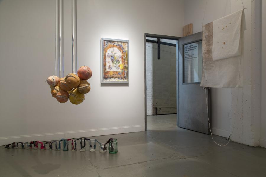 an orange and plexi rod ceiling hung sculpture with other floor and ceiling sculptures in the background 