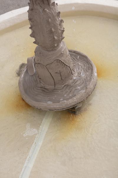 detail image of the base of a fountain floor sculpture made of clay with water at the base