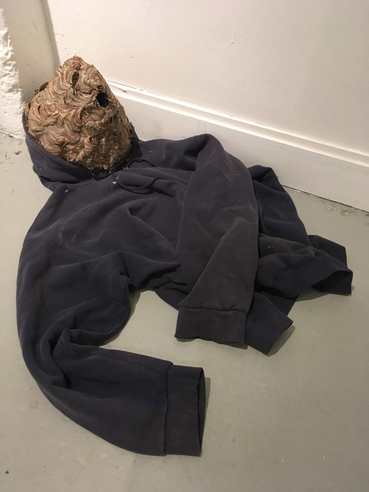 floor sculpture combining hooded sweatshirt and wasp nest