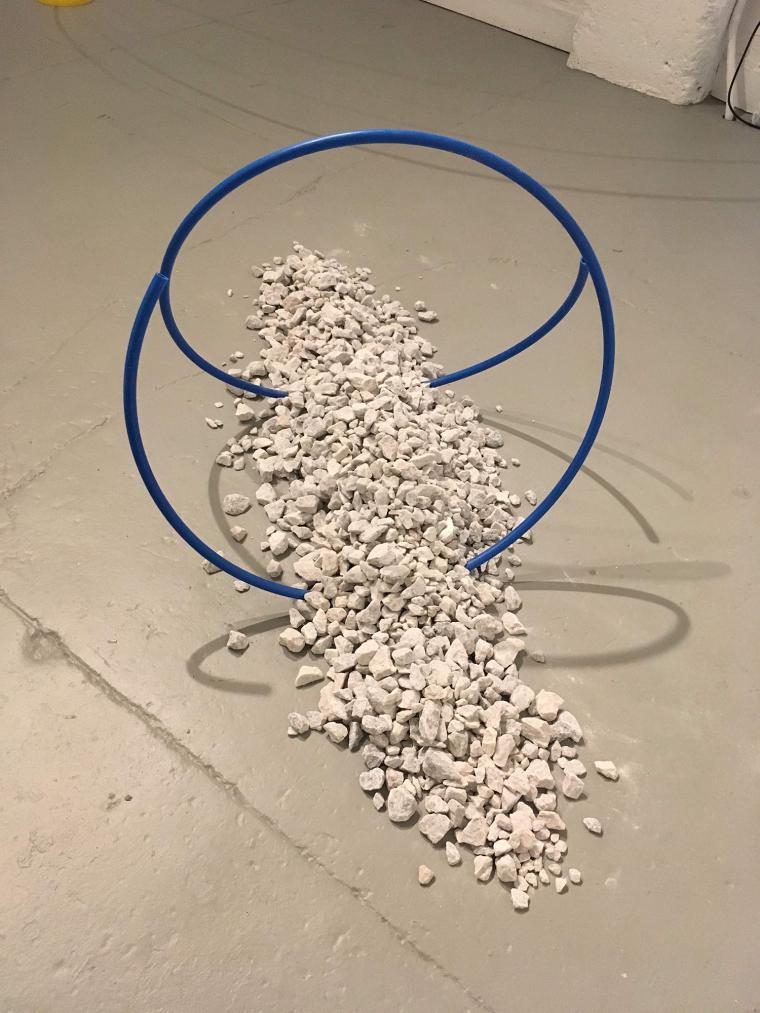 floor sculpture combining grey gravel poured in a line supporting a looping blue tube