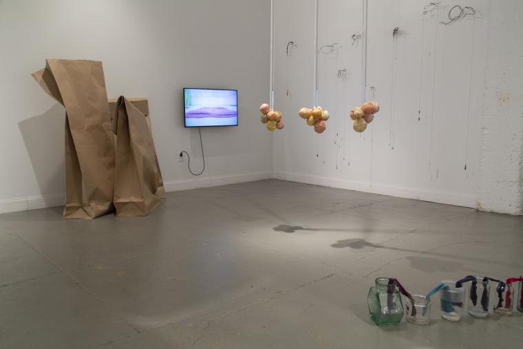 installation image of multiple pieces including large paper bag sculptures, a video monitor, sculptures hanging from the ceiling