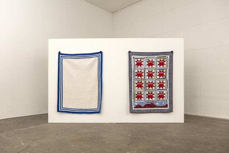 Two quilts hung on wall. One is blank white while the other has a grid of red eight pointed stars